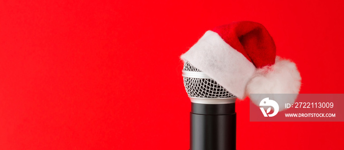 microphone with a Santa hat on a red background, Christmas songs, holidays, events, events. New Year’s greetings. Festive Christmas banner background