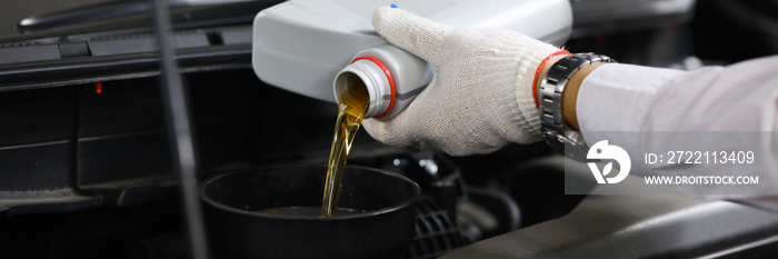 Focus on auto mechanic in gloves replacing and pouring fresh oil into engine at automobile service station. Vehicle inspection concept. Blurred background