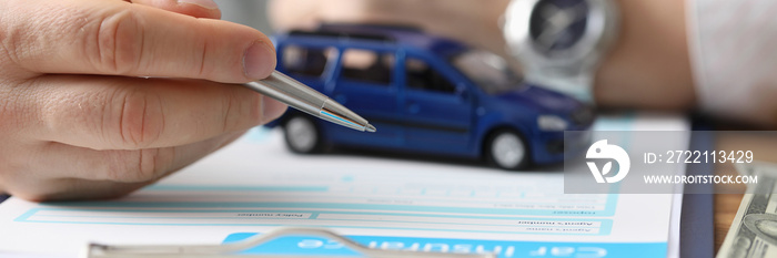 Male hands hold ballpoint pen over car insurance blank and toy car. Car insurance concept.