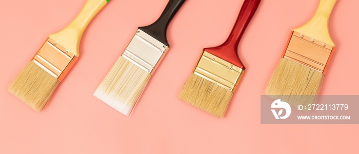 Four paint brushes lined up on a pink background.