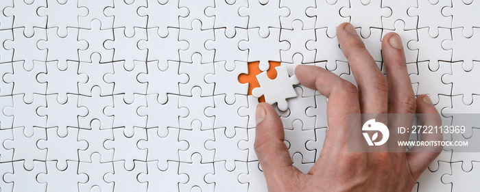 The texture of a white jigsaw puzzle in the assembled state with one missing element that the male hand puts in