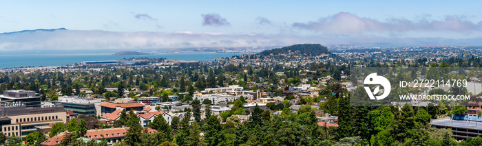 View towards Berkeley, Richmond and the San Francisco bay area shoreline on a sunny day; University of California Berkeley campus buildings in the foreground, California