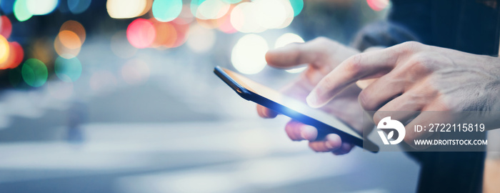 Closeup image of male hands with smartphone at night on city street, searching internet or social networks, hipster man typing an sms message on chat