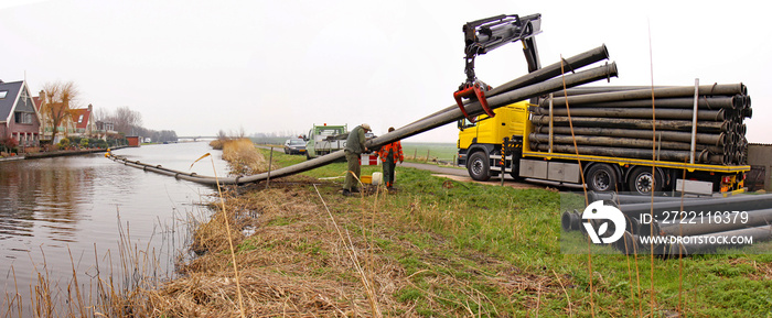 Technicians disassembling a pipeline. A truck-mounted crane pulls the pipe from a canal, while two others unscrew the pipe sections.