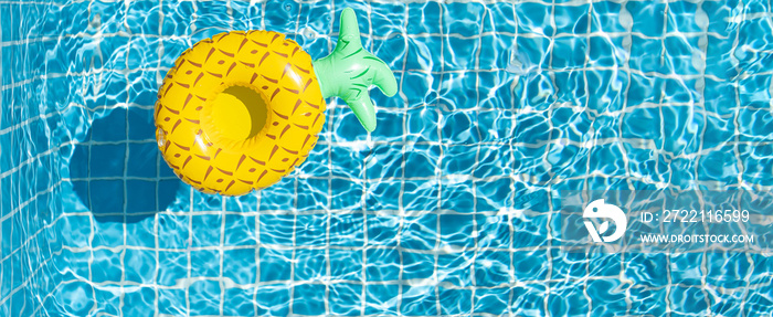 Yellow pineapple ring floating in blue swimming pool at sunny day. Inflatable ring, rest and summer vacation concept