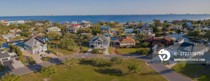 Intracoastal neighborhood with single-family homes at Navarre, Florida. Panoramic aerial view of street at the front of houses with waterways in between against the bay and sky background.