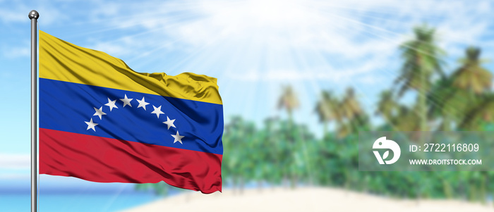 Waving Venezuela flag in the sunny blue sky with summer beach background. Vacation theme, holiday concept.