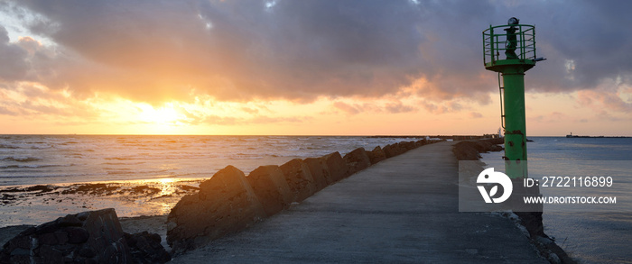 Old pier (walkway, promenade) to the lighthouse. Breakwaters close-up. Clear blue sky, pink sunset clouds, golden sunlight. Seascape, cloudscape. Baltic sea. Spring. Tourism, landmark, navigation