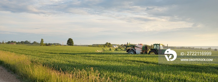 Modern tractor with irrigation system working on a green plowed agricultural field at sunset. Summer rural scene. Environment, special equipment, technology, farm industry