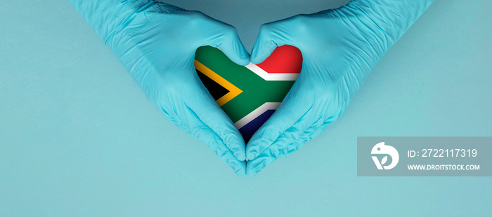 Doctors hands wearing blue surgical gloves making hear shape symbol with south africa flag