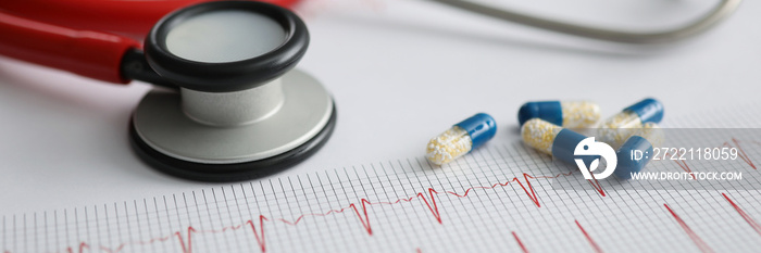 Medical capsules and red stethoscope lying on electrocardiogram closeup