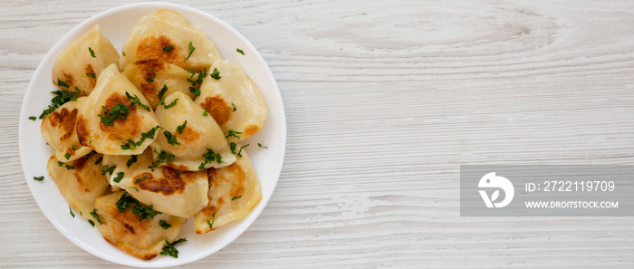 Homemade traditional polish fried potato pierogis on a white plate on a white wooden surface, top view. From above, flat lay, overhead. Space for text.