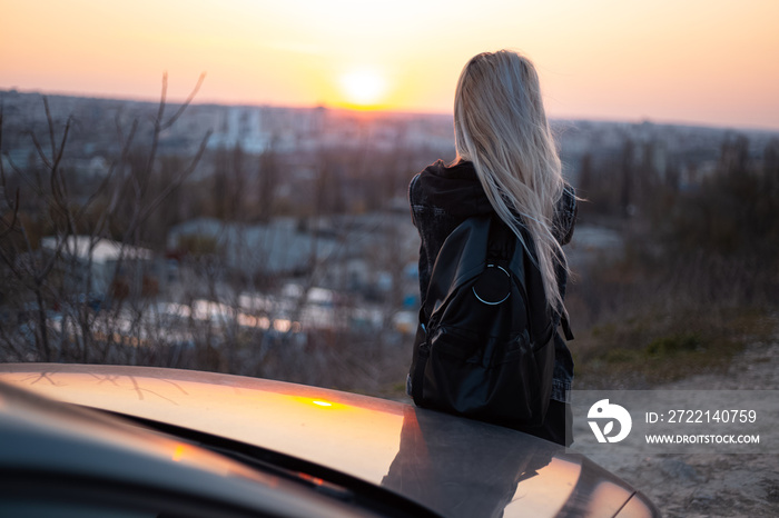 Back view of young girl with black backpack looks at the sunset.