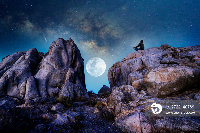 silhouette of a person on the rock outdoors meditating or praying at night under the Milky Way and full Moon