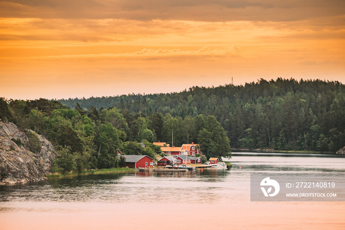 Sweden. Many Beautiful Red Swedish Wooden Log Cabins Houses On Rocky Island Coast In Summer Evening. Lake Or River Landscape.