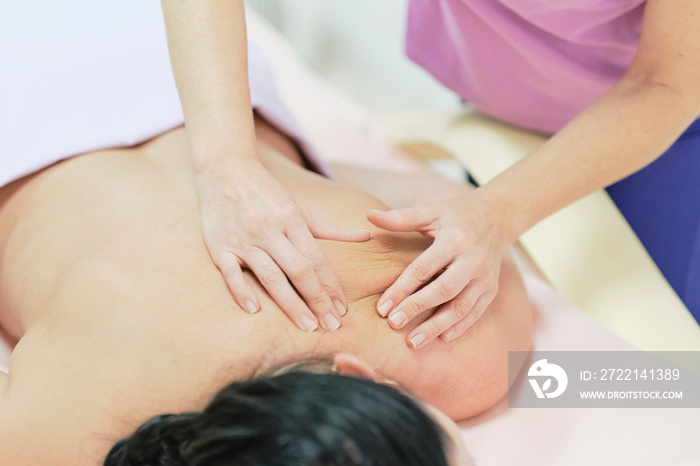 Physical Therapist Massaging the Back and Shoulder of a Female Patient. Over shoulder view of masseur performing deep tissue massage of womens back to release pain