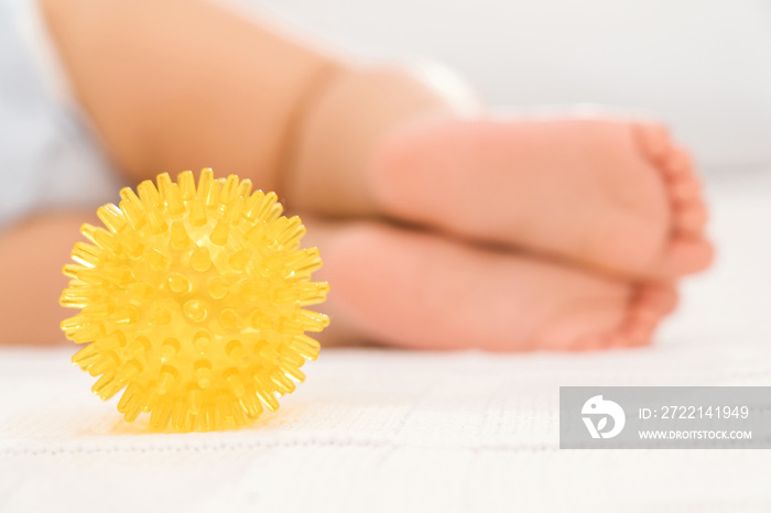 A yellow massage ball and the legs of a sleeping baby in the background. Selective focus. The concept of baby massage