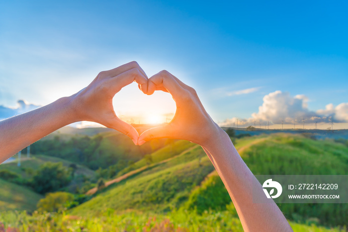 Female hands in the form of heart against sunlight behind landsc