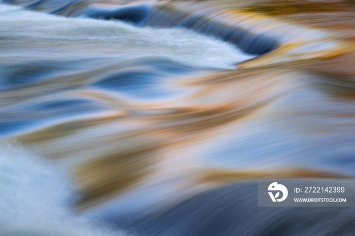 Landscape of a Bond Falls rapids captured with motion blur and illuminated by reflected color from sunlit autumn maples and blue sky overhead, Ottawa National Forest, Michigan’s Upper Peninsula, USA