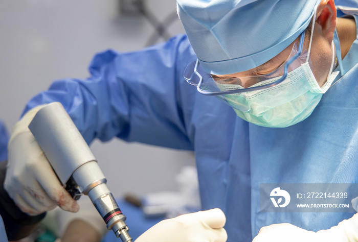 Close up photo of orthopaedic surgeon inside operating room. Doctor in blue surgical gown suit intense perform orthopaedic surgery with team of assistants.Medical concept.