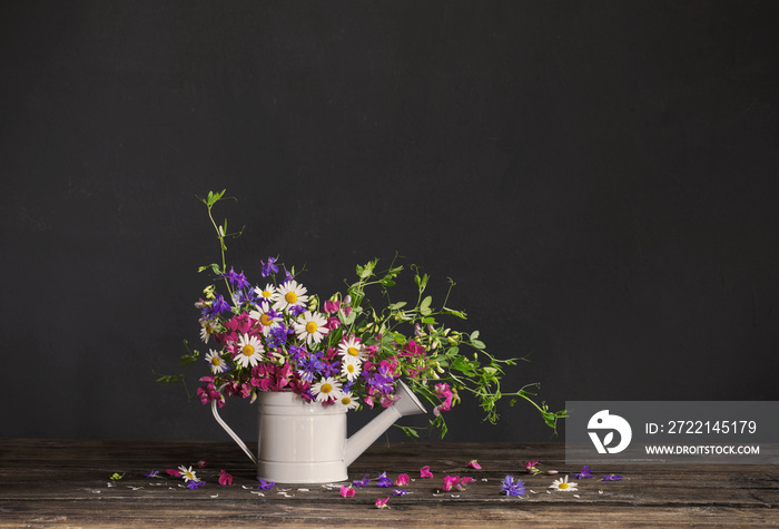 wild summer flowers in watering can on dark background