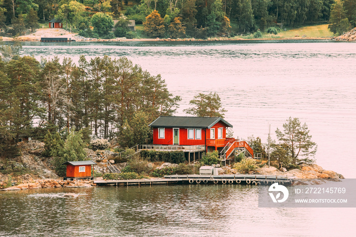 Sweden. Many Beautiful Red Swedish Wooden Log Cabin House On Rocky Island Coast In Summer. Lake Or River Landscape