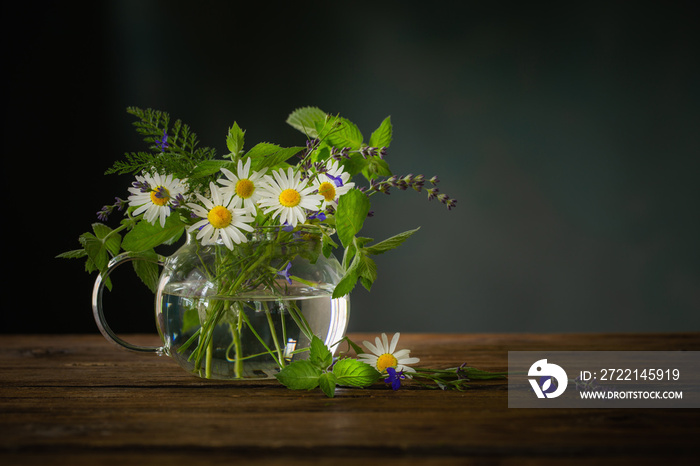 bouquet of summer flowers in  glass teapot on  dark background,  concept of healthy herbal tea