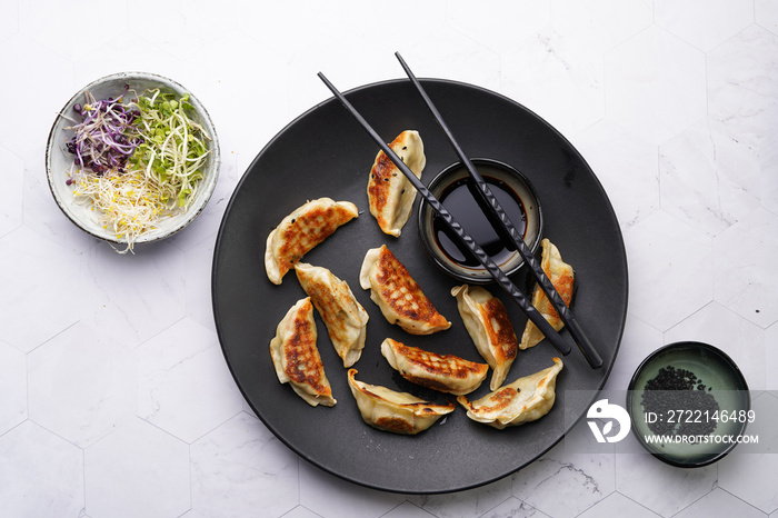 Japanese dumplings gyoza stuffed with chicken meat on a black plate with soy sauce, microgreens, sesame seeds and black chop sticks