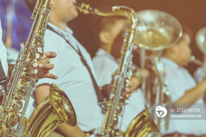 Male student with friends blow the saxophone with the band for performance on stage at night.