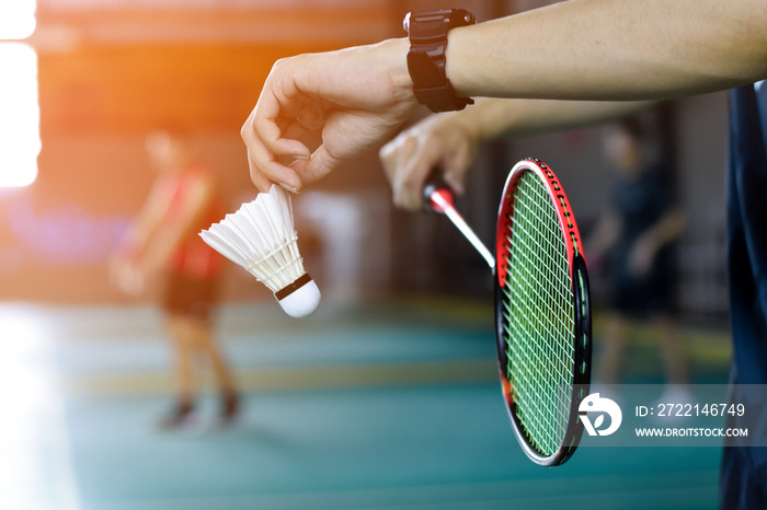 Badminton player holds racket and white cream shuttlecock in front of the net before serving it to another side of the court.