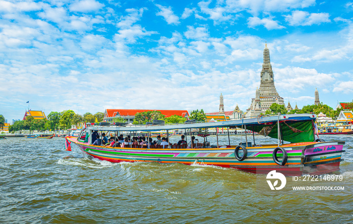 View over river Chao Phraya from boat back to temple Wat Arun, eldest temple in Bangkok. In foreground is speed longboat passing. Behind are tour boats and ferries.