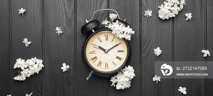 Alarm clock and lilac flowers on dark wooden background. Spring time