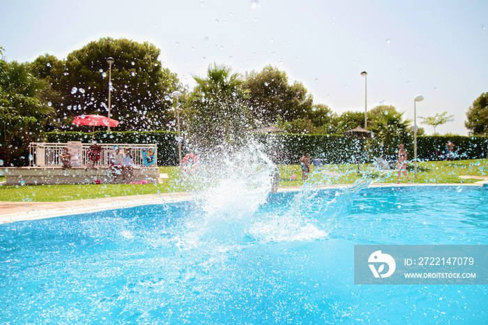 Kid jumping into a pool creating a giant water splash. Beautiful weather, summertime ! Very bright and colorful shot, clear blue water. Beautiful sunny day. Alcossebre, Valencia Community, Spain