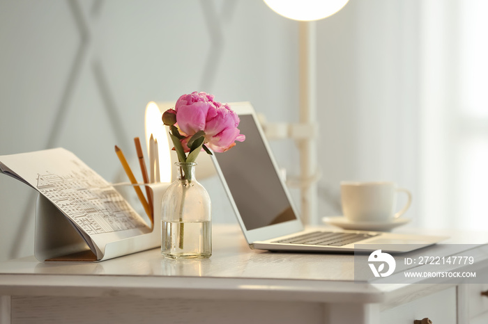 Vase with beautiful flowers and laptop on table in room