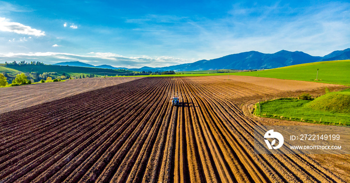 Farmer in tractor preparing land with seedbed cultivator in farmlands. Tractor plows a field. Agricultural work in processing, cultivation of land. Furrows row patter.aerial photo