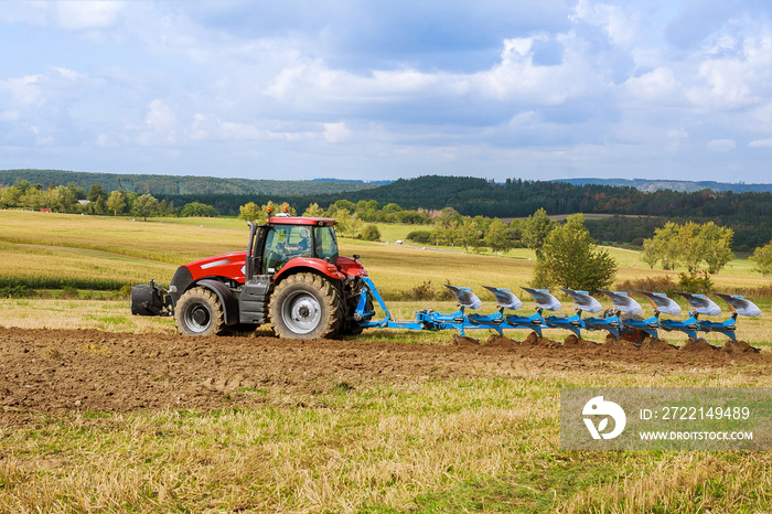 A tractor with a large plow plows a field. Tractor with agricultural attachment.