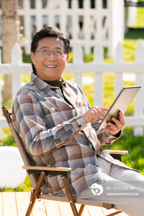 一个老年男人坐在露营院子里看平板电脑