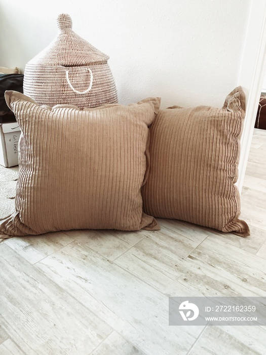 Two brown pillows and a basket on the ground in a white room