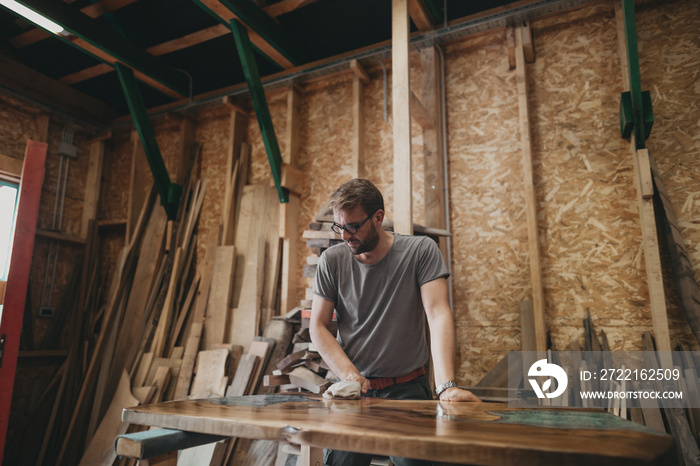 Artisan Carpenter Working in his Workshop, putting Oil on Epoxy Table