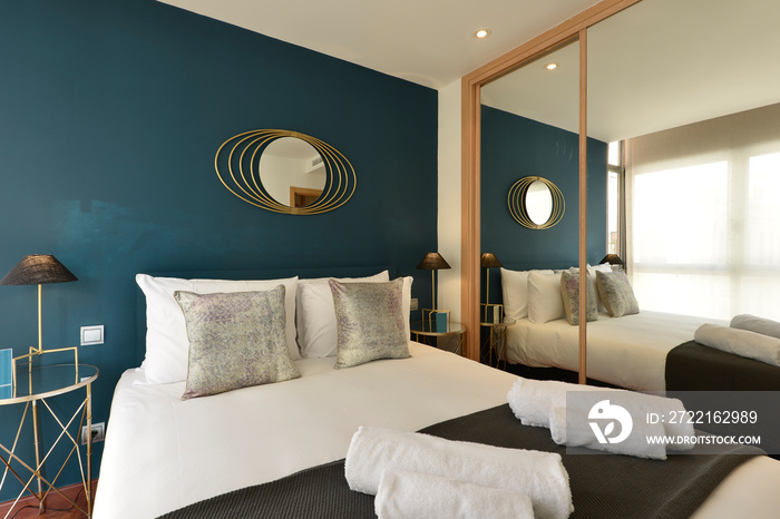 Bedroom with silver cushions, blue colored wall, fitted wardrobe with mirrored sliding doors and mat