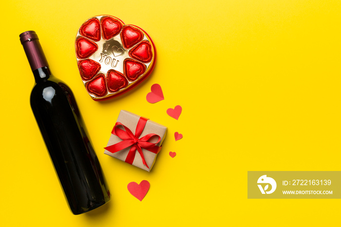 Bottle of red wine on colored background for Valentine Day with gift and chocolate. Heart shaped wit