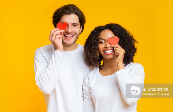 Portrait of happy interracial couple with red paper hearts over eyes