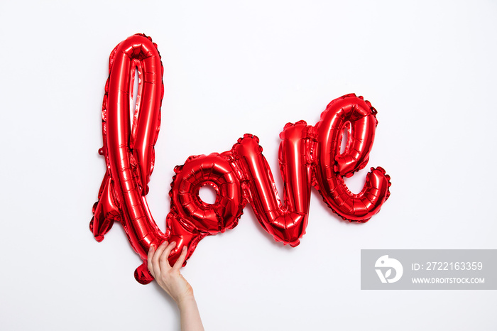 Red foil Love balloon held against a plain white background