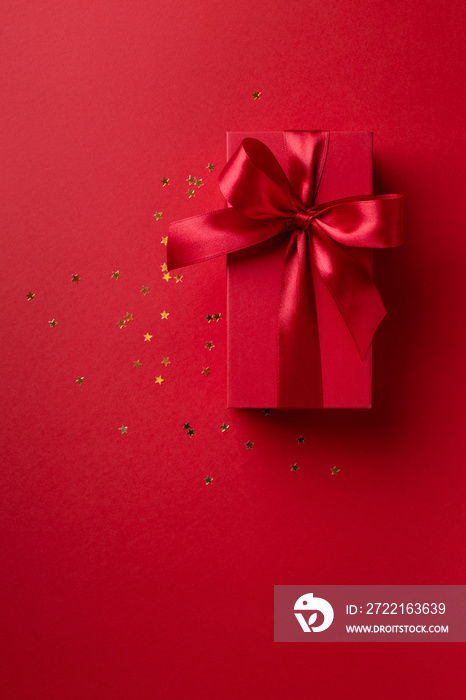 Red gift box for Christmas or Valentines day with golden confetti on red background .