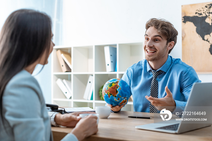 cheerful travel agent holding globe while talking to client