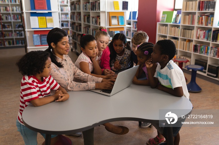 Female teacher teaching schoolkids on laptop at table in school