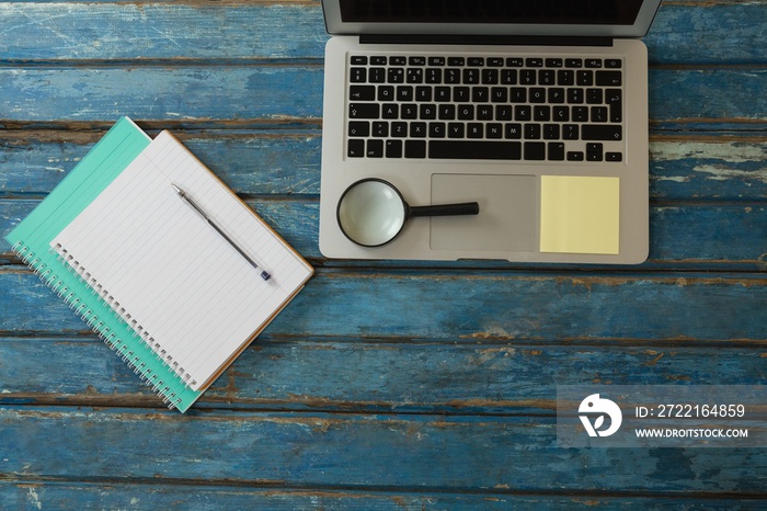 Blank book, pen, magnifying glass and laptop on wooden plank