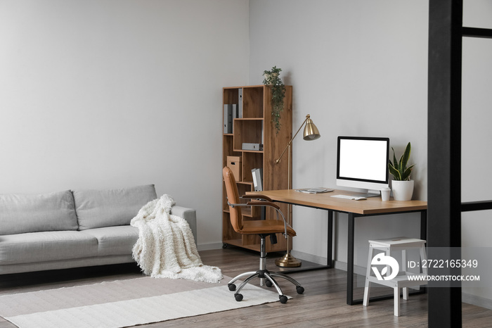 Interior of light office with table, modern computer and shelving unit