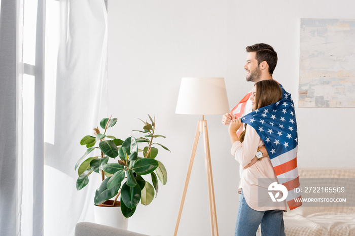 side view of young couple covered with american flag standing at home