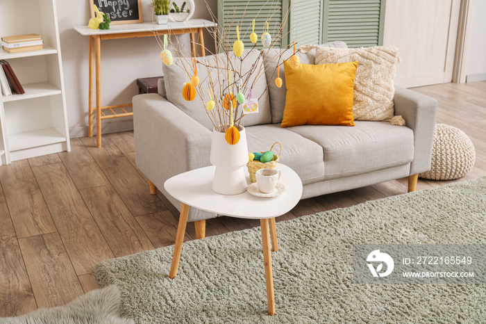 Vase with tree branches, Easter eggs and coffee cup on table in interior of living room